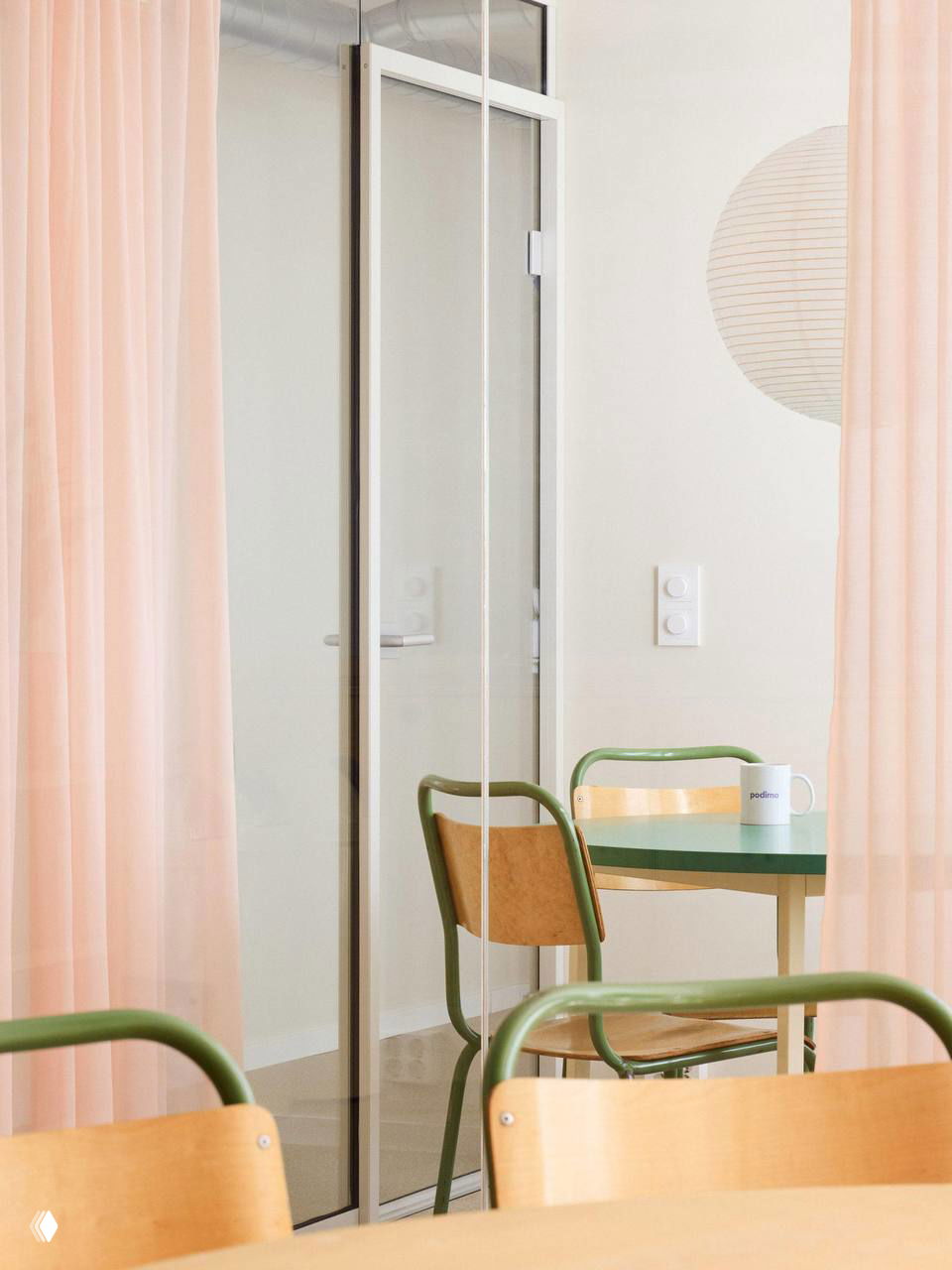 Кафе-зона или столовая: стеклянные двери, светло-розовые шторы и столы с зелёными стульями, создающие спокойный уголок внутри яркого офиса.