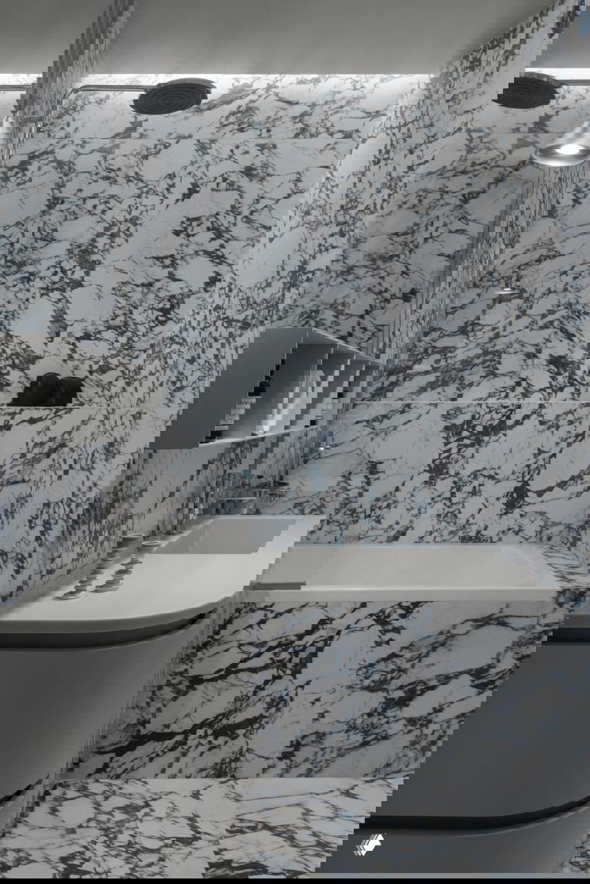 Ванная комната облицована выразительным бело‑синим мрамором: ванна, раковина и настенные плоскости с ярким рисунком камня создают декоративный контраст на фоне серого дома.