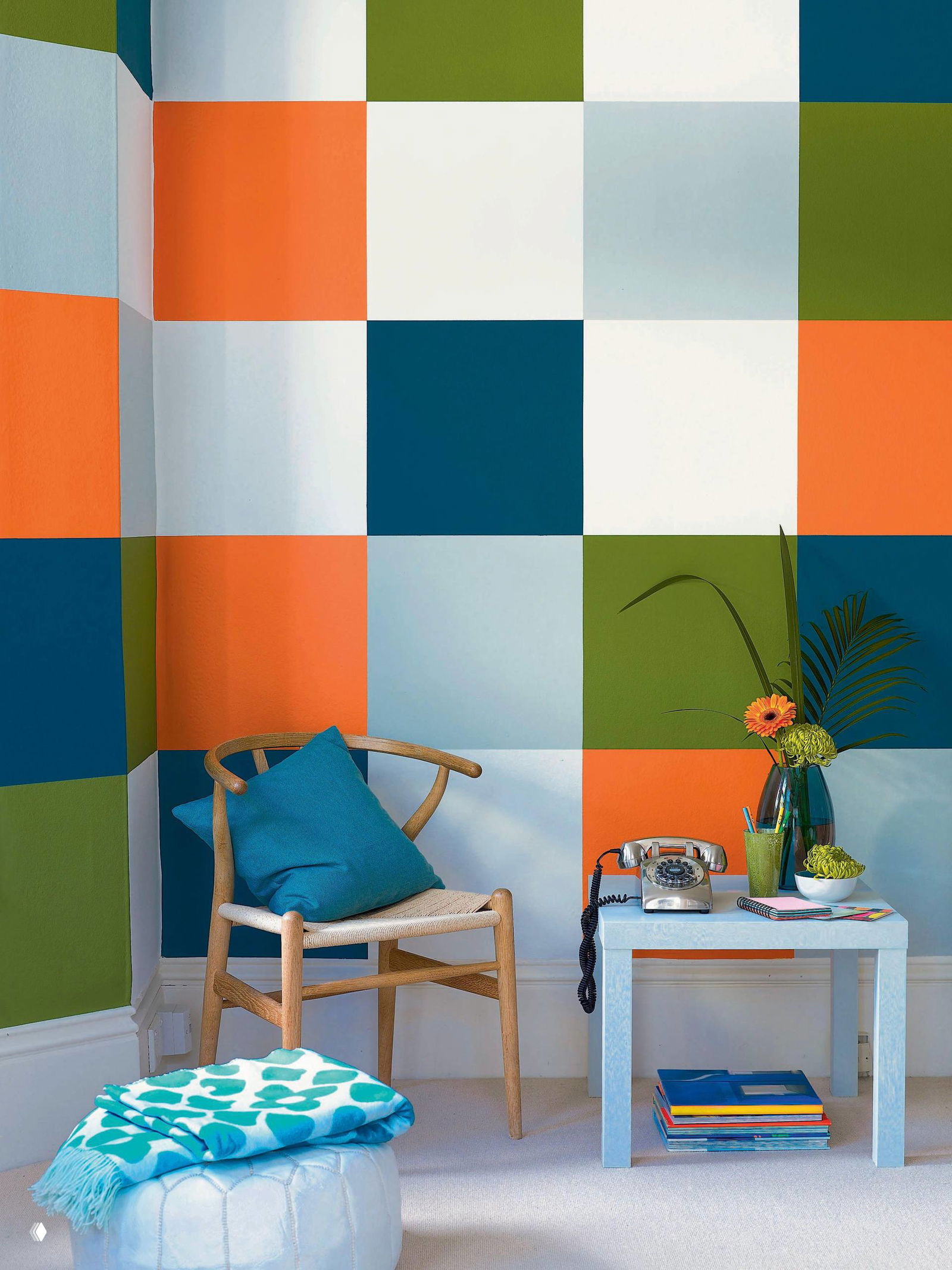 Интерьерный фрагмент с крупной клеткой из разноцветных квадратов на стене, кресло и небольшой столик создают яркий акцент в комнате.