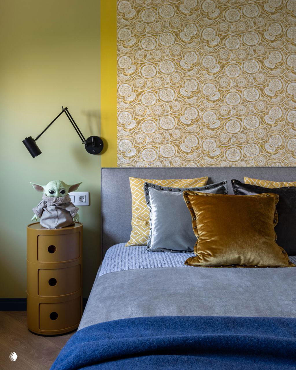 Интерьер подростковой комнаты с акцентной желтой вставкой над изголовьем, подушки разной фактуры и декоративный прикроватный столик в стиле ретро.