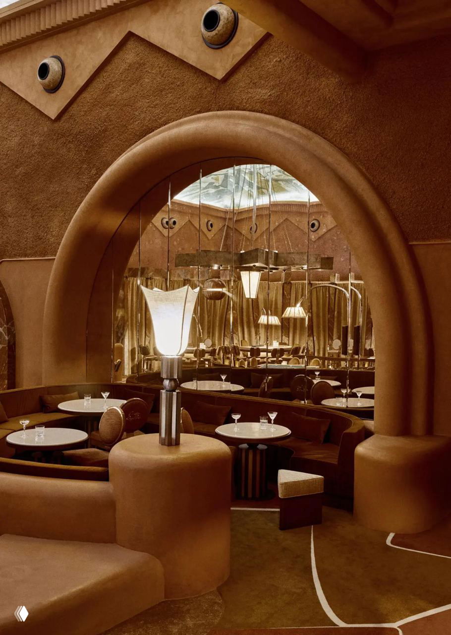 Уютная лаундж-зона с арочным проходом и зеркалами, мягкие округлые диваны и низкие столики в неомавританском декоре.