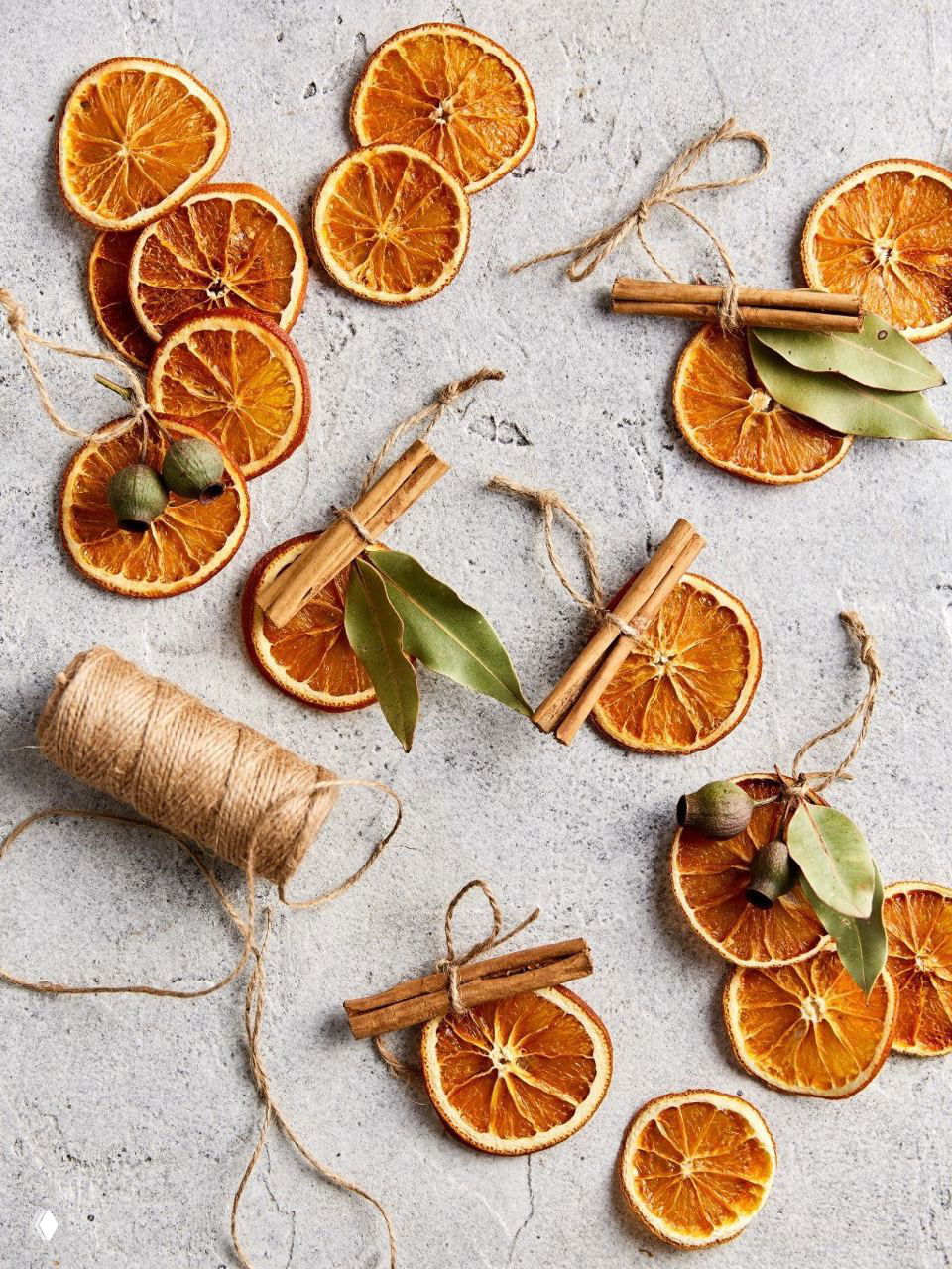 Крупный план сушёных апельсиновых кружочков, связанных джутовой ниткой и дополненных палочками корицы — натуральный декор для ёлочных украшений и подарков.