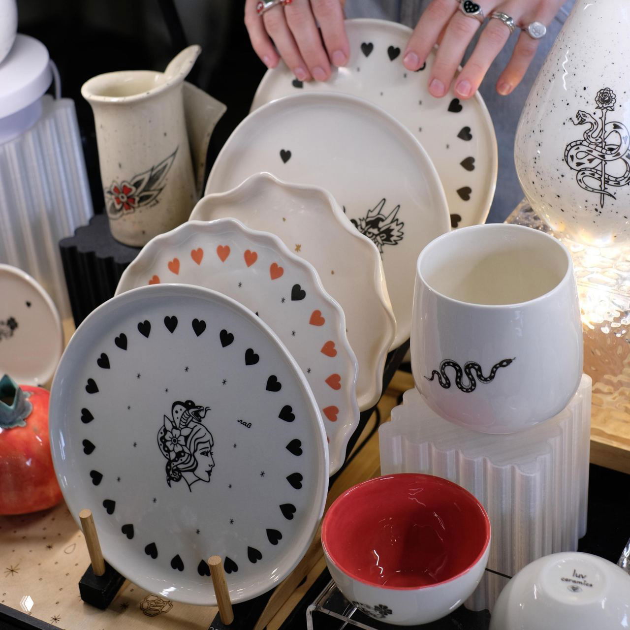 Набор декоративных фарфоровых тарелок и чаш с графическими рисунками и сердечками, аккуратно выставленных на стенде — примеры изделий мастеров маркета.