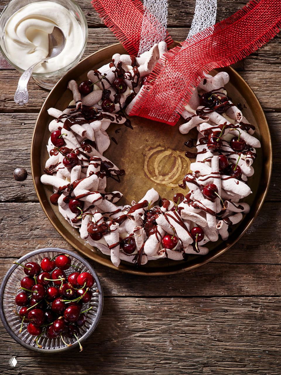 Пышный венок из безе, политый шоколадом и украшенный вишнями; праздничная съедобная композиция на деревянном фоне с текстурой.