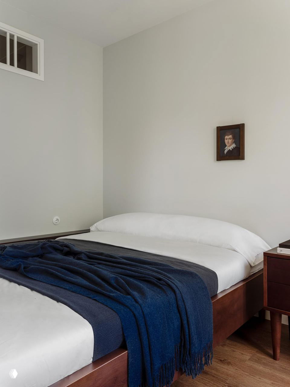 Спальня с низкой деревянной кроватью и белым постельным бельём, на кровати тёмно-синий плед — спокойная цветовая гамма и минимализм в декоре.