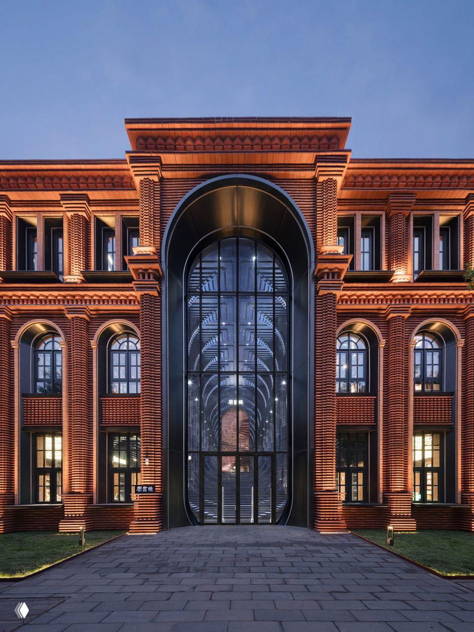 Фасад книжного магазина: строгий кирпичный корпус с арочными проёмами и крупным чёрным входом-порталом, подчёркивающим контраст материалов и форму здания.