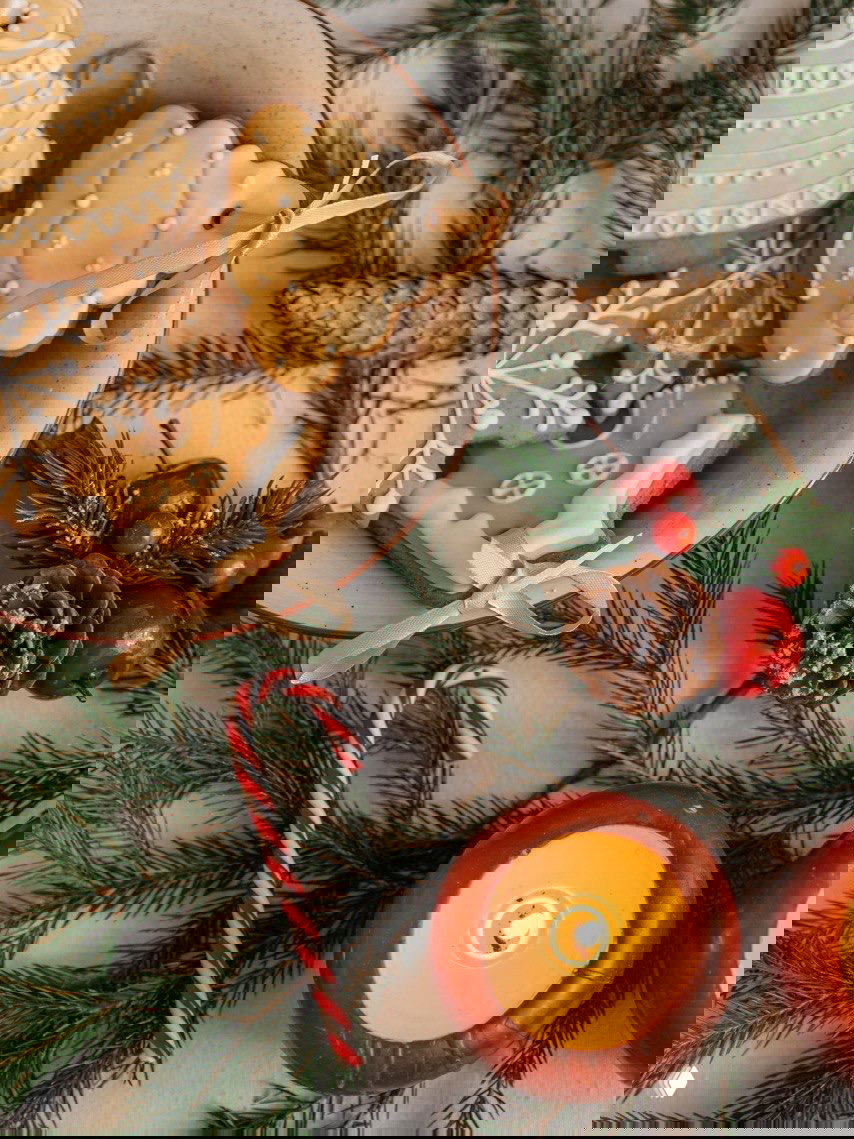 Тарелка с имбирными пряниками, украшенными белой глазурью, рядом зелёные веточки хвои, тросточка и свеча — элементы для праздничной сервировки и ёлочных игрушек.