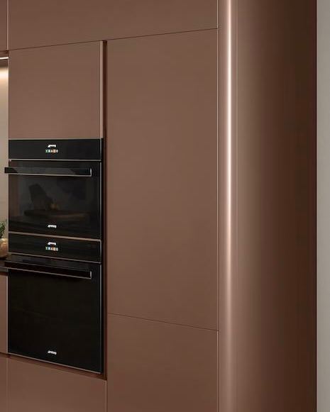 Вертикальный кадр в коричневых тонах: встроенные модули и духовые шкафы, подчёркивающие монохромную фактуру фасадов и минималистичный профиль.