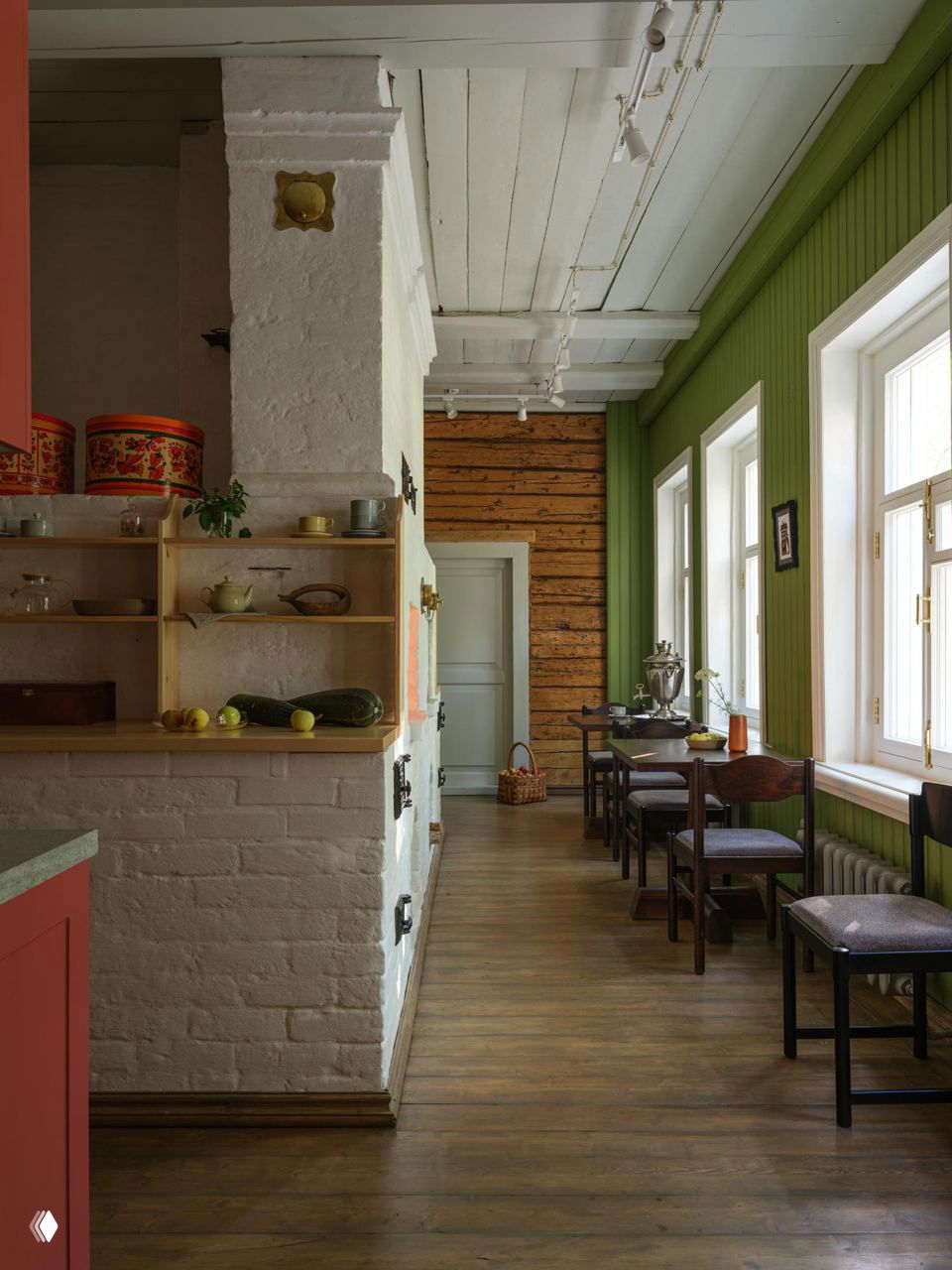 Длинный внутренний коридор с белой печью и зелёными стеновыми панелями, деревянный пол и обстановка в стиле начала XX века в отеле.