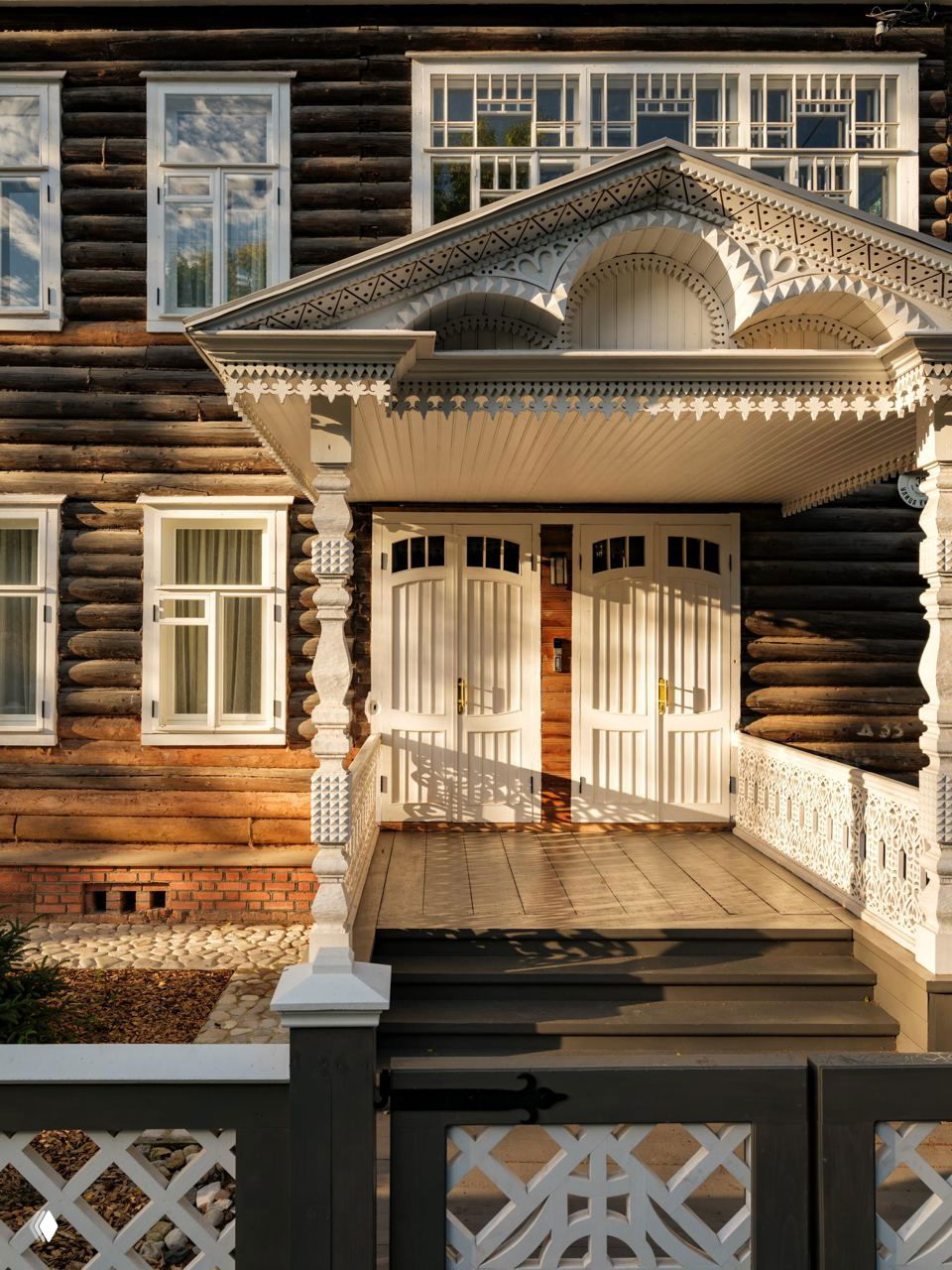 Вход в отреставрированный деревянный дом в Вологде с белыми резными наличниками, двойными дверями и крыльцом в тёплом вечернем свете.