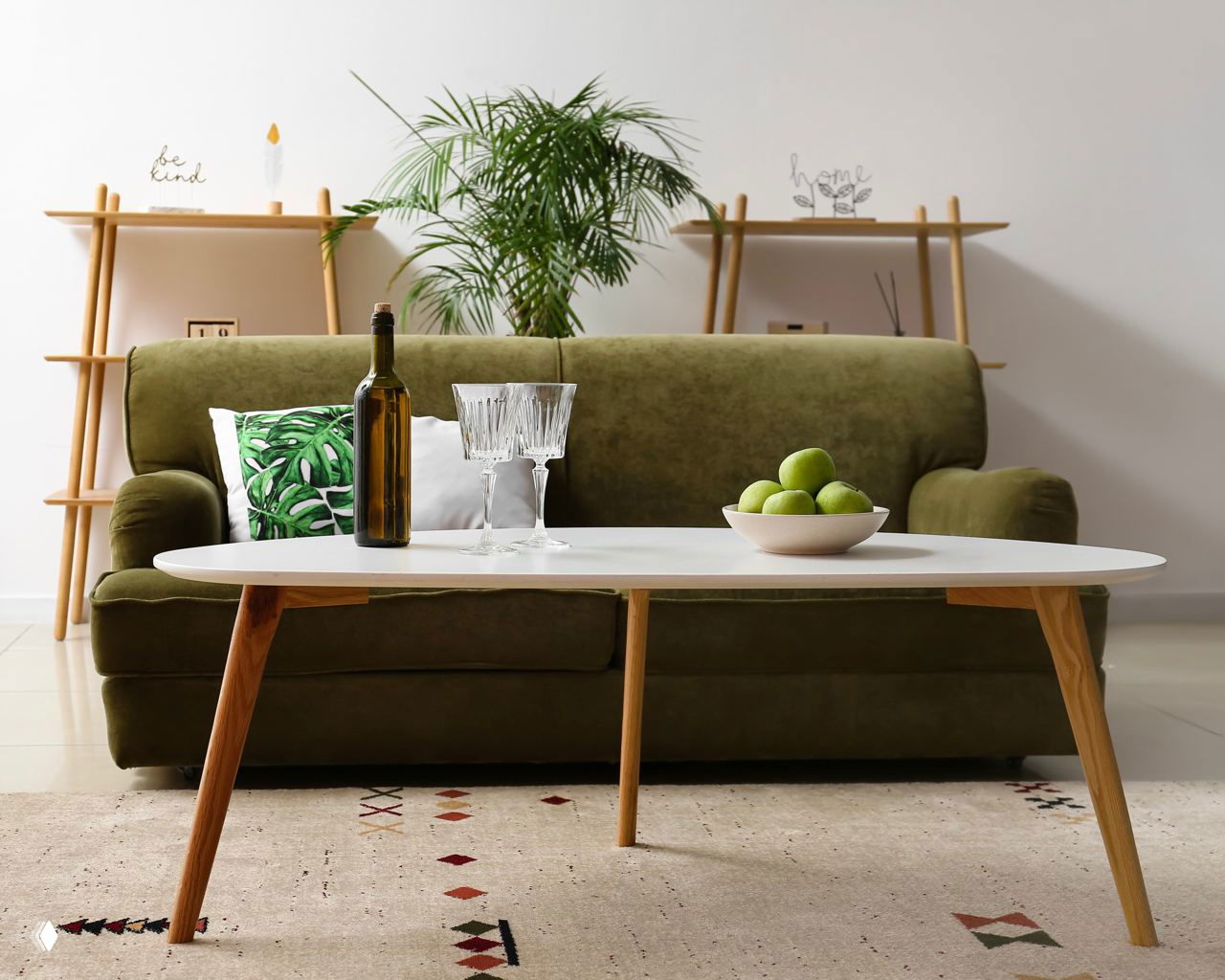 Оливковый диван за низким столиком, на полу ковер с геометрическим рисунком; кадр показывает интерьер, требующий регулярного ухода и чистки покрытий.