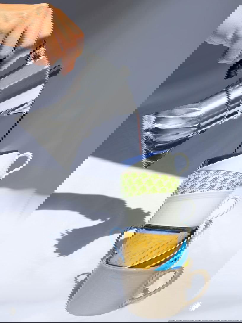 Крупный план процесса наливания кофе из Turbo Moka в стопку разноцветных чашек, видна форма корпуса и наклон наливания, динамичная композиция.