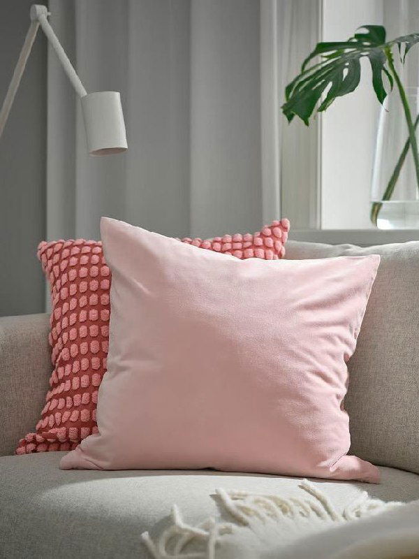 Розовые декоративные подушки на светлом диване: передняя гладкая подушка и текстурная задняя в другом оттенке Rebel Pink, рядом видно зелёное растение.