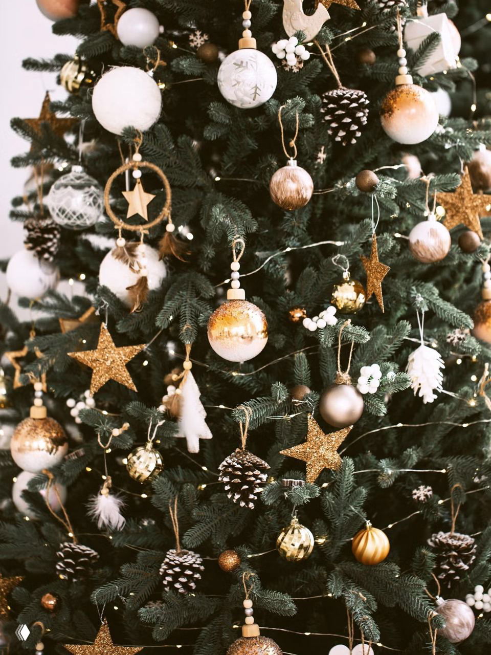 Украшенная ёлка с бело‑золотыми шарами, блестящими звёздами и шишками в роли подвесных игрушек — праздничный декоративный натюрморт для вдохновения.