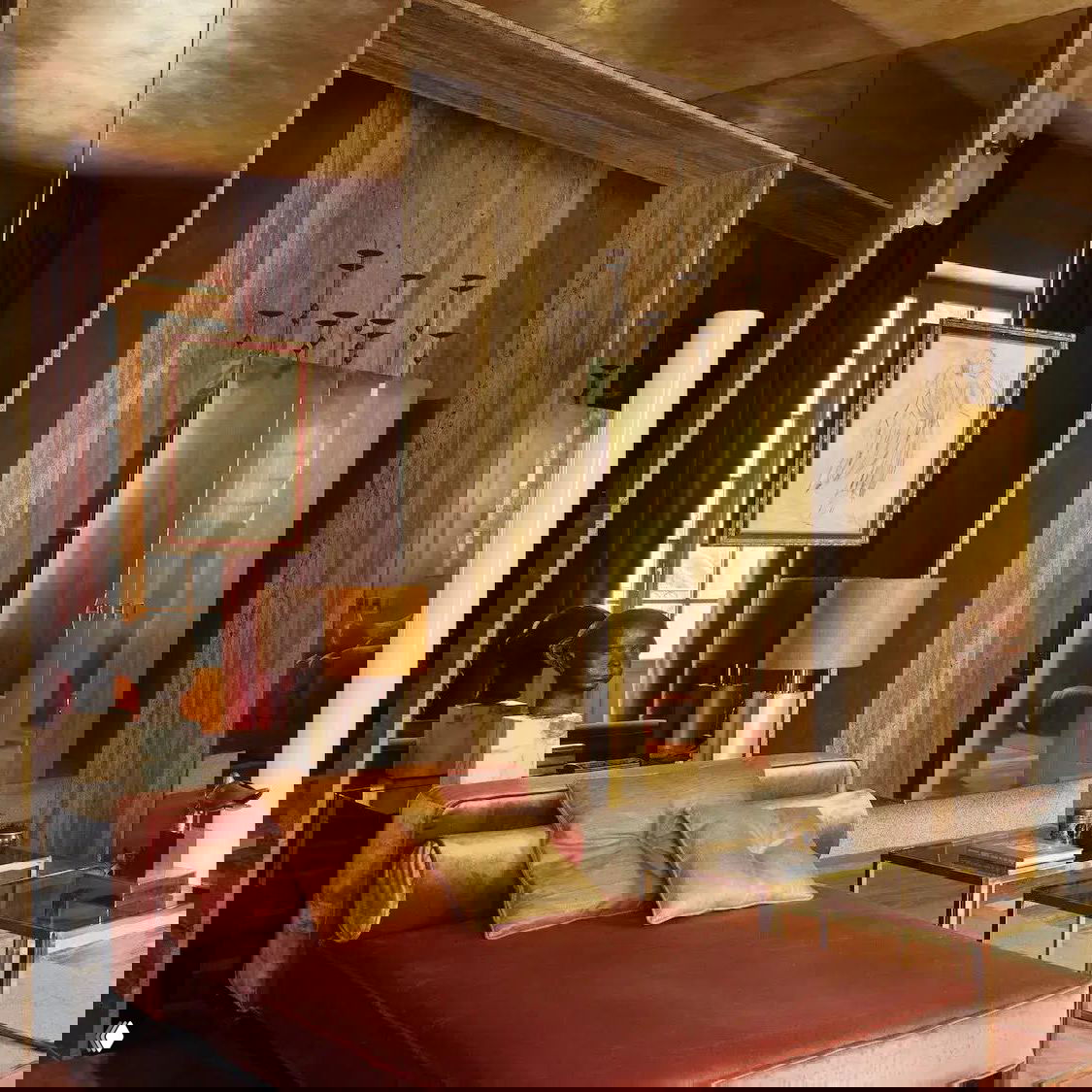 Комната с бархатным шезлонгом тёплого красно-терракотового оттенка, латунные элементы и большое зеркало в резной раме создают роскошную атмосферу.