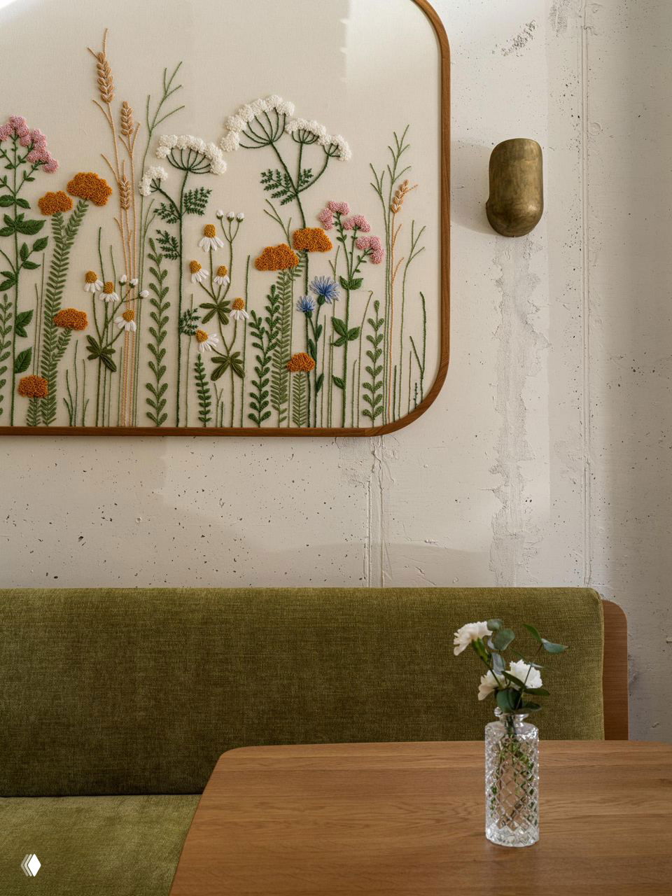 Крупный фрагмент вышитого панно в технике punch needle с изображением полевых цветов, текстура стежков хорошо различима на нейтральном фоне стены.