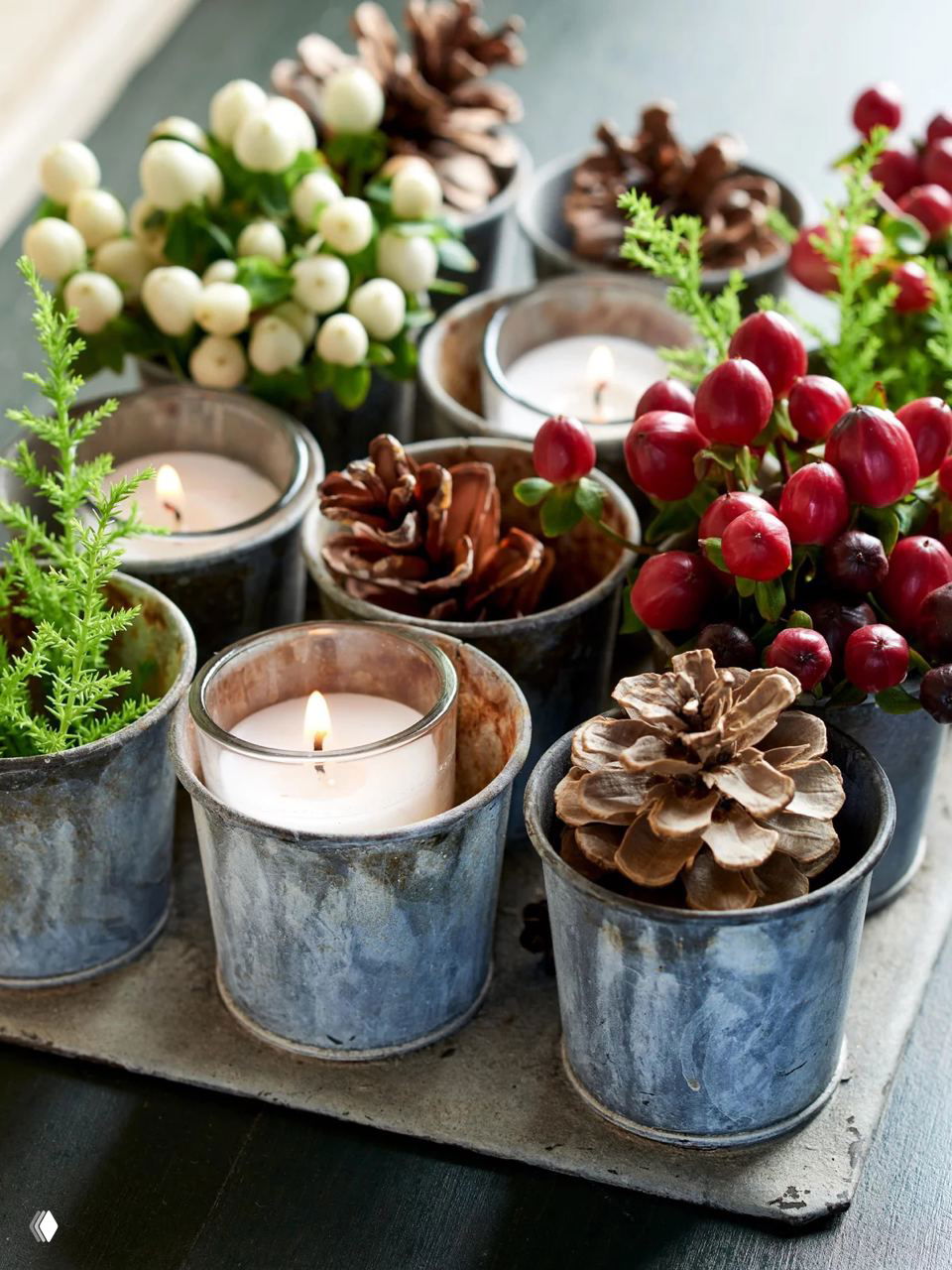 Небольшая композиция с чашами и горящими свечами, среди декора расположены шишки и ягодные веточки для уютного праздничного оформления стола.