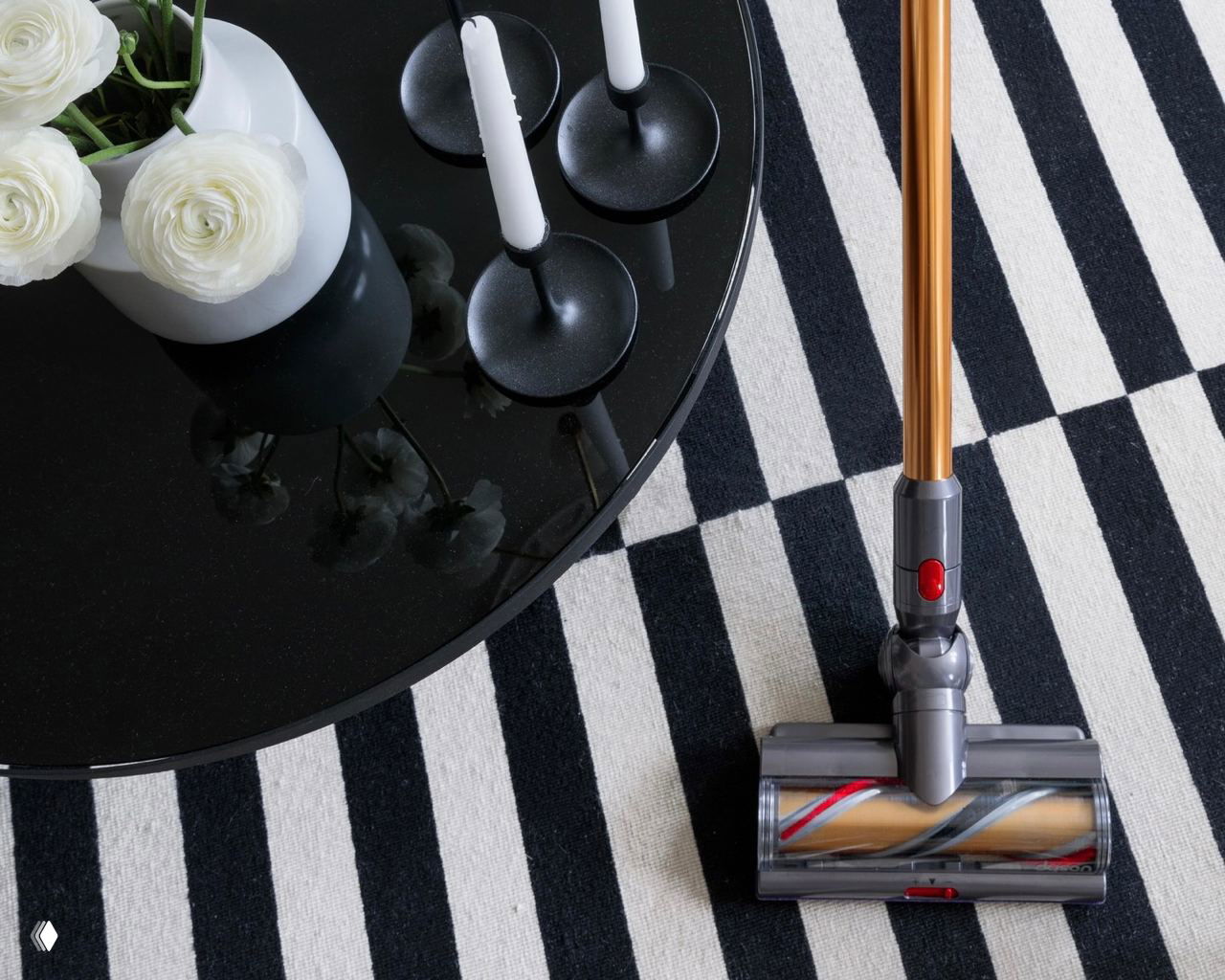 Фрагмент ковра в чёрно‑белую полоску и рабочая насадка пылесоса на полу; демонстрация процесса уборки и применения техники для ухода за ковром.