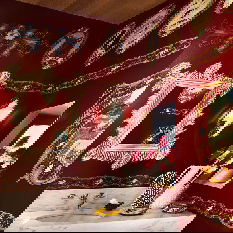 Яркая ванная комната с бордовыми стенами, золотыми рамами и декоративными медальонами; богатая отделка и мраморная столешница подчёркивают стиль Boom Boom.