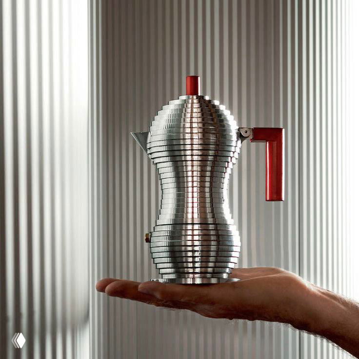 Металлическая кофеварка в руке на нейтральном фоне — предметный объект с выраженными деталями отделки и ручки, демонстрация промышленного дизайна.