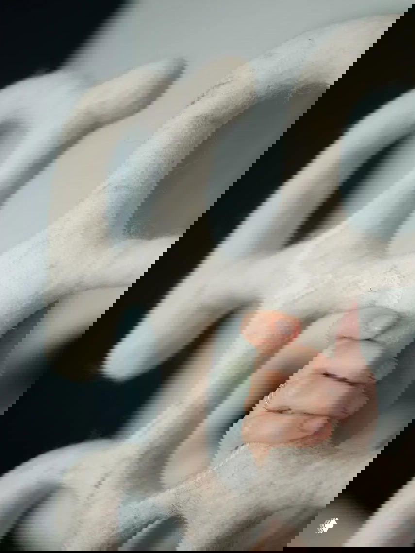 Крупный план руки, удерживающей пуховую структуру из белого войлока с выраженной фактурой, видны волокна и плотность материала.