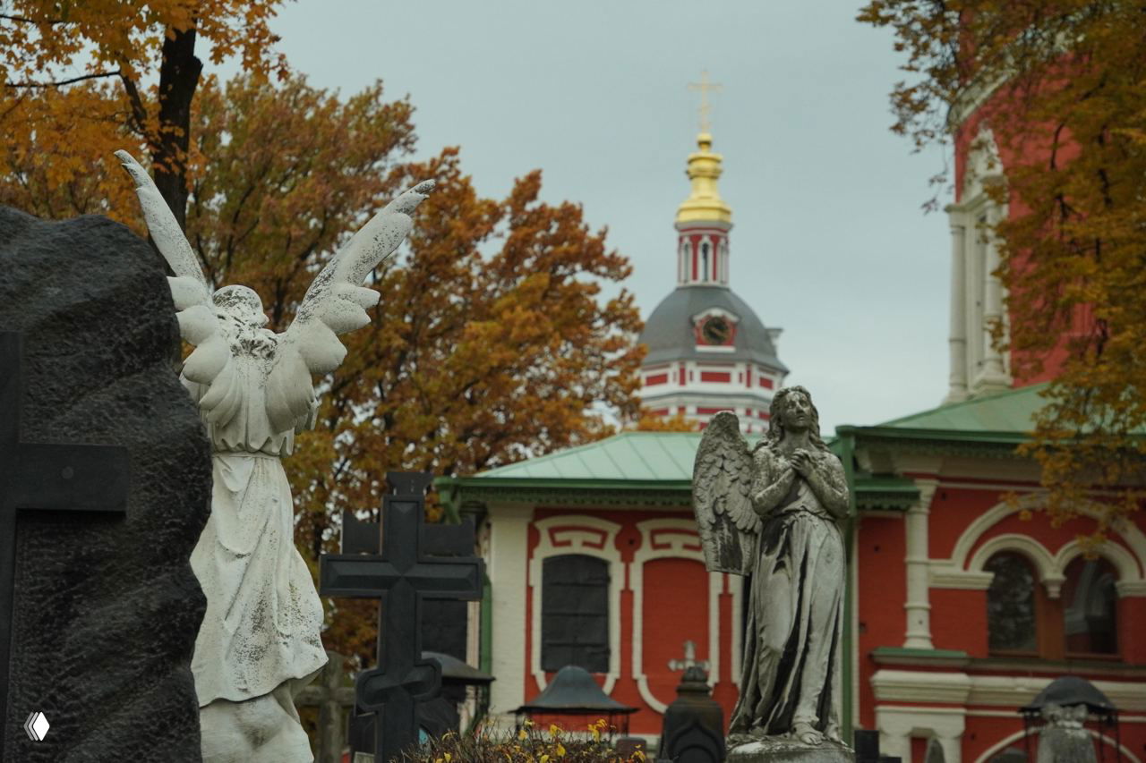 Надгробные статуи ангелов и плакальщиц на Донском кладбище на фоне куполов монастыря, осенняя листва и старые кресты вокруг