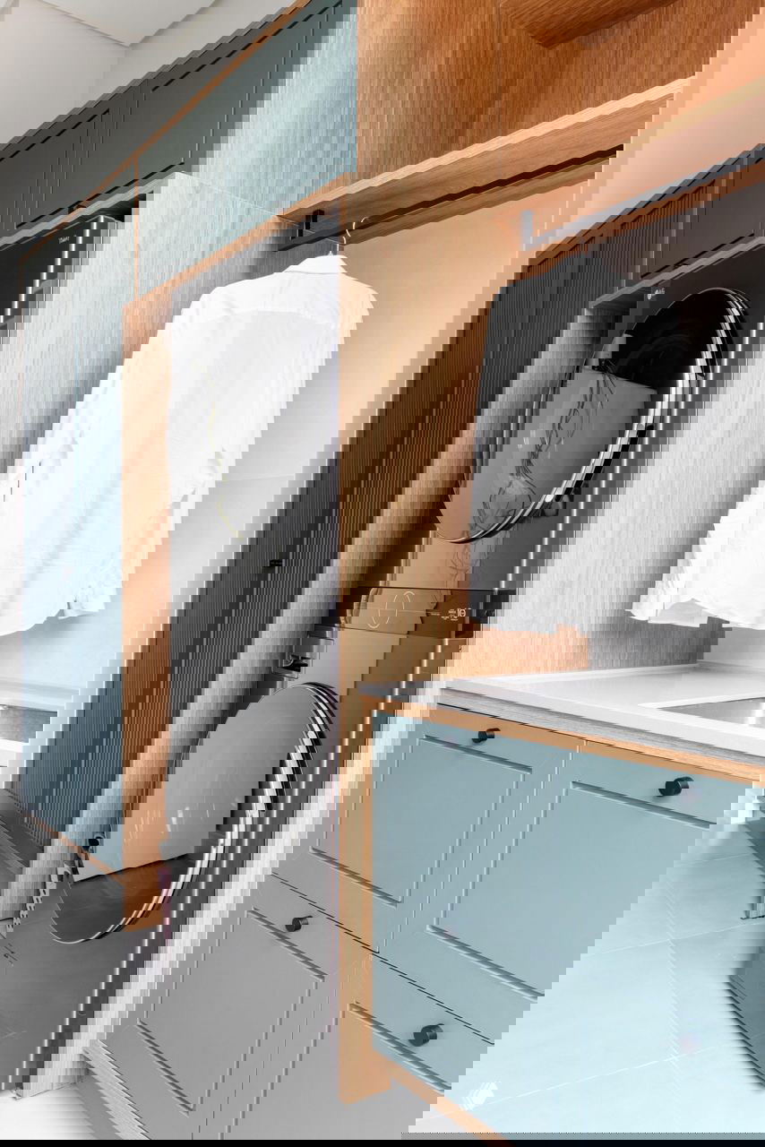 Прачечная с нишей для стиральной и сушильной машины в колонне, бирюзовые фасады шкафов и столешница с мойкой в светлой отделке.