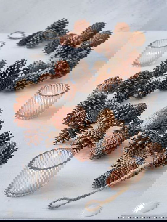 Гирлянда из натуральных шишек, разложенная с подсвечниками на светлой поверхности, фото демонстрирует простую идею рождественской композиции из шишек.