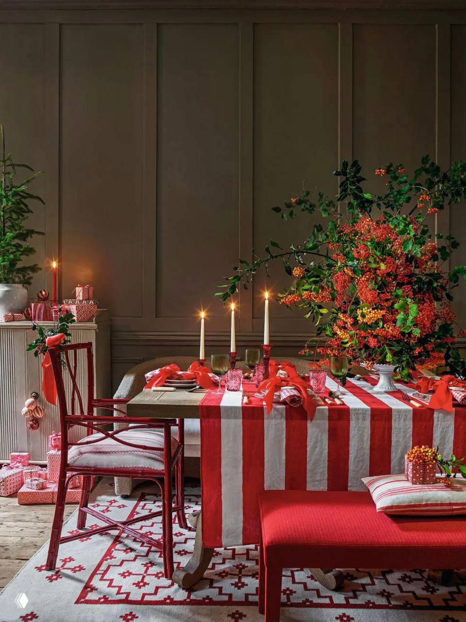 Красно‑белая сервировка с полосатой скатертью: стол украшен свечами, пышной цветочной композицией и яркими текстильными акцентами в праздничной гамме.
