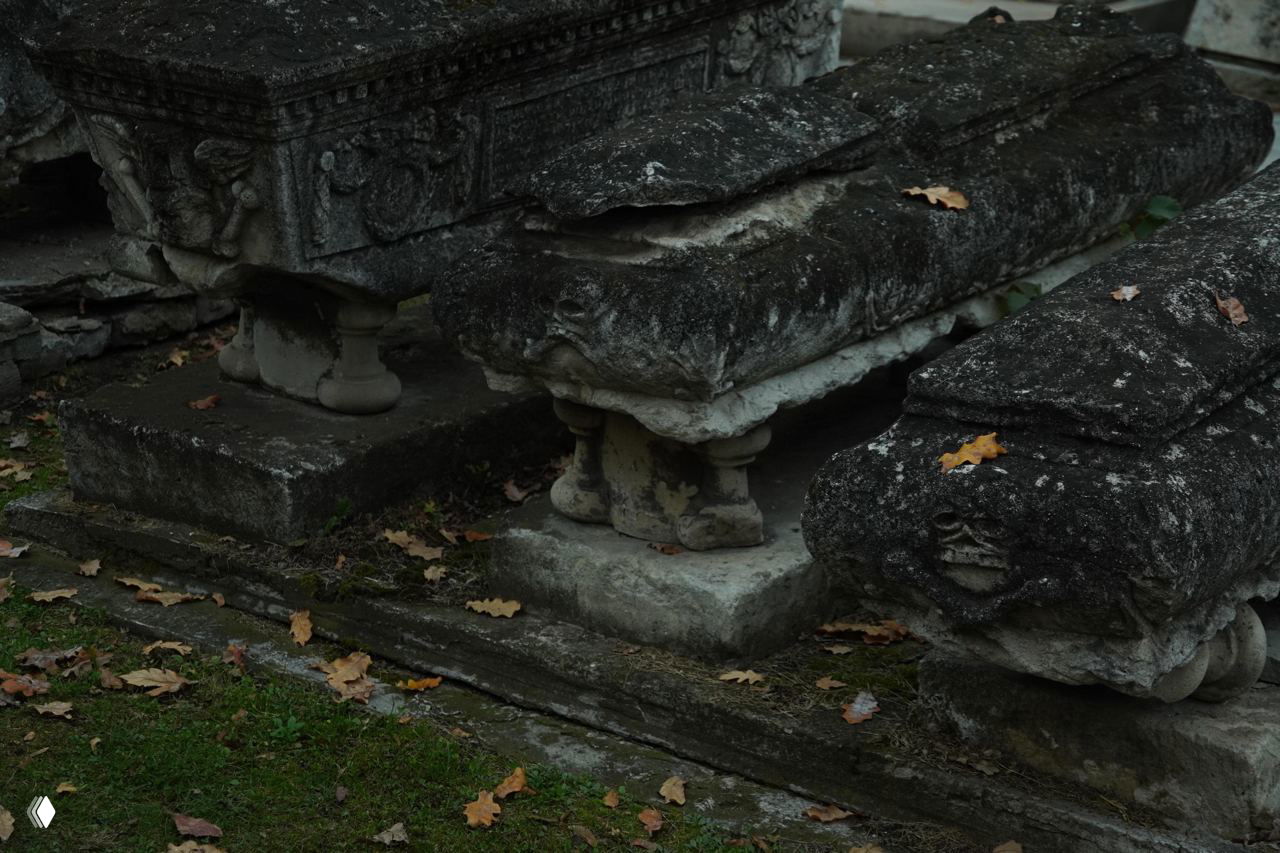 Каменные саркофаги и плиты с потемневшей поверхностью на Донском кладбище, опавшие листья лежат на старом камне