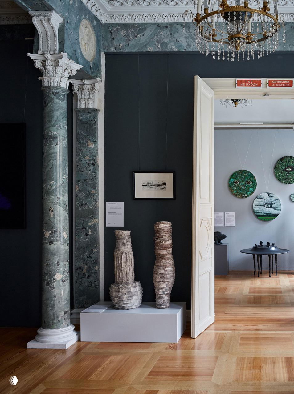 Выставочная сцена: две войлочные вазы на подиуме в музейном интерьере с колоннами и декоративными рельефами, экспозиционная подача работ.