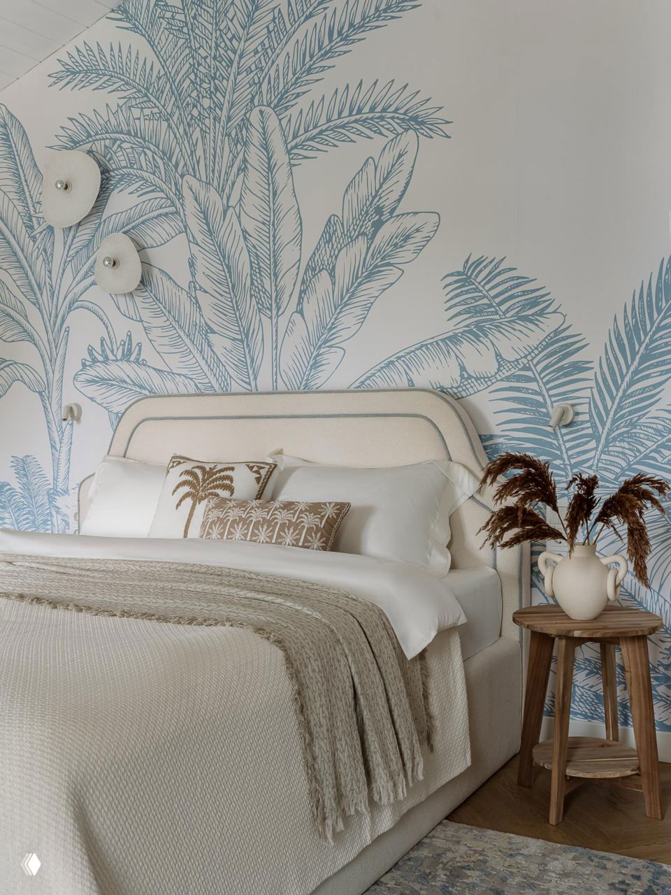 Спальня в мягких бежевых тонах с изголовьем и крупным растительным принтом на стене в голубых оттенках — текстильные и керамические акценты.
