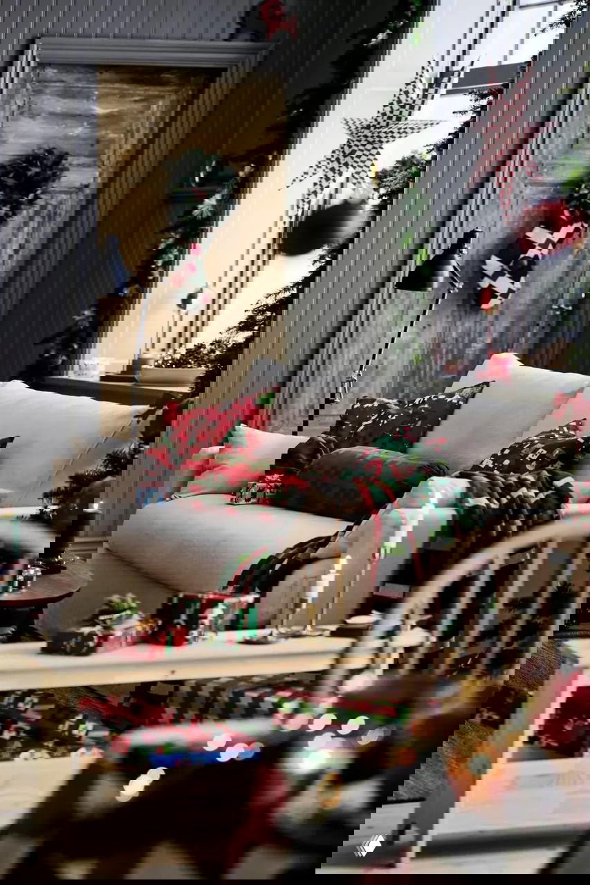 Уютная гостиная с бежевым диваном, подушками и пледом в красно‑зелёную клетку на фоне состаренной двери и рождественского декора