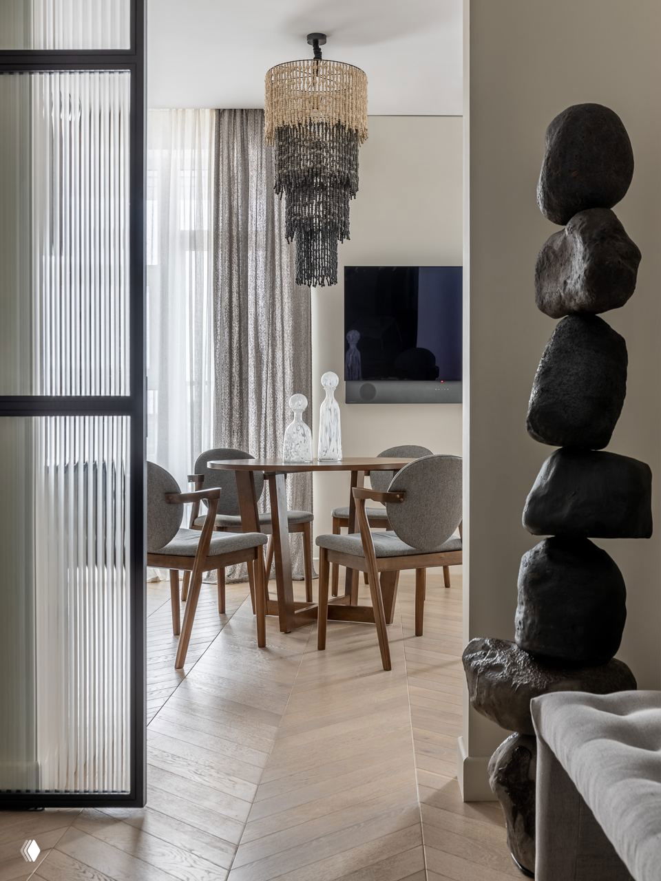 Обеденная зона и стулья в скандинавском стиле, крупная висящая люстра и декоративная инсталляция из камней у прохода, вид из гостиной на столовую.