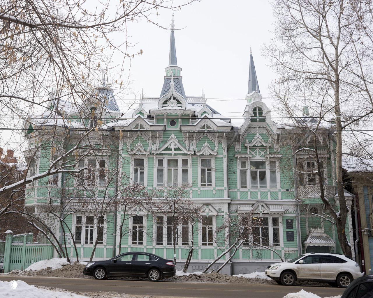 Зелёно-бирюзовый двухэтажный деревянный особняк в Томске с башенками и декором в снеговом пейзаже — пример архитектуры конца XIX — начала XX века.
