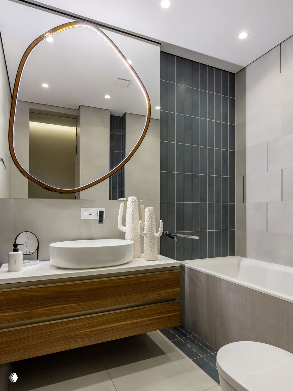Ванная комната в современном стиле: округлое зеркало, белая раковина и деревянная тумба на фоне графичных плиток серого тона и ванны.