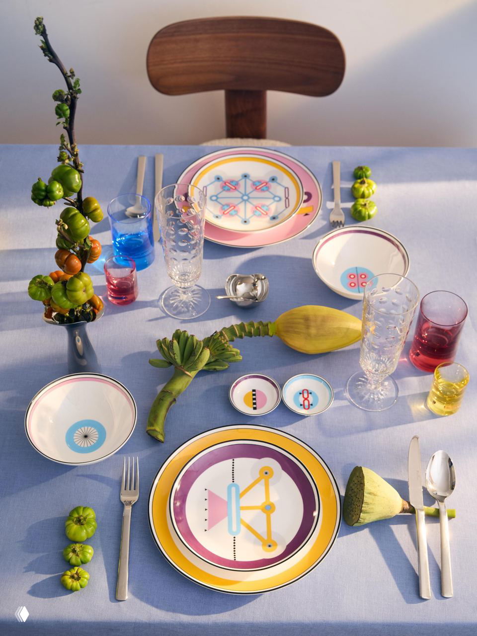 Ярко сервированный стол с тарелками из коллекции Shirokov «Мемфис»: геометрические и цветные узоры, хрустальные бокалы и декоративные детали в светлой композиции.