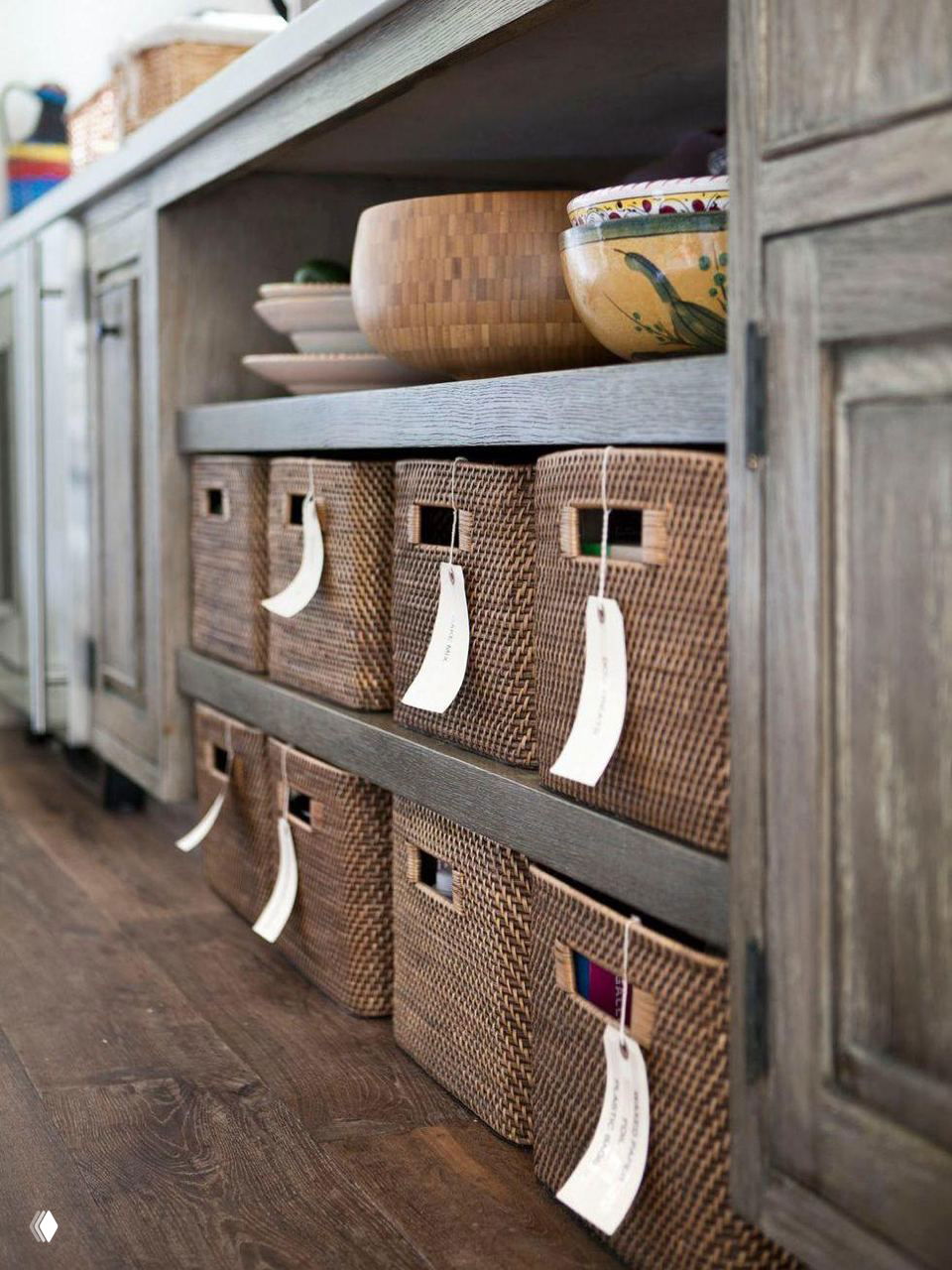Плетёные коричневые корзины с подвесными ярлыками, аккуратно размещённые в низкой открытой полке — идея для маркировки и компактного хранения вещей.
