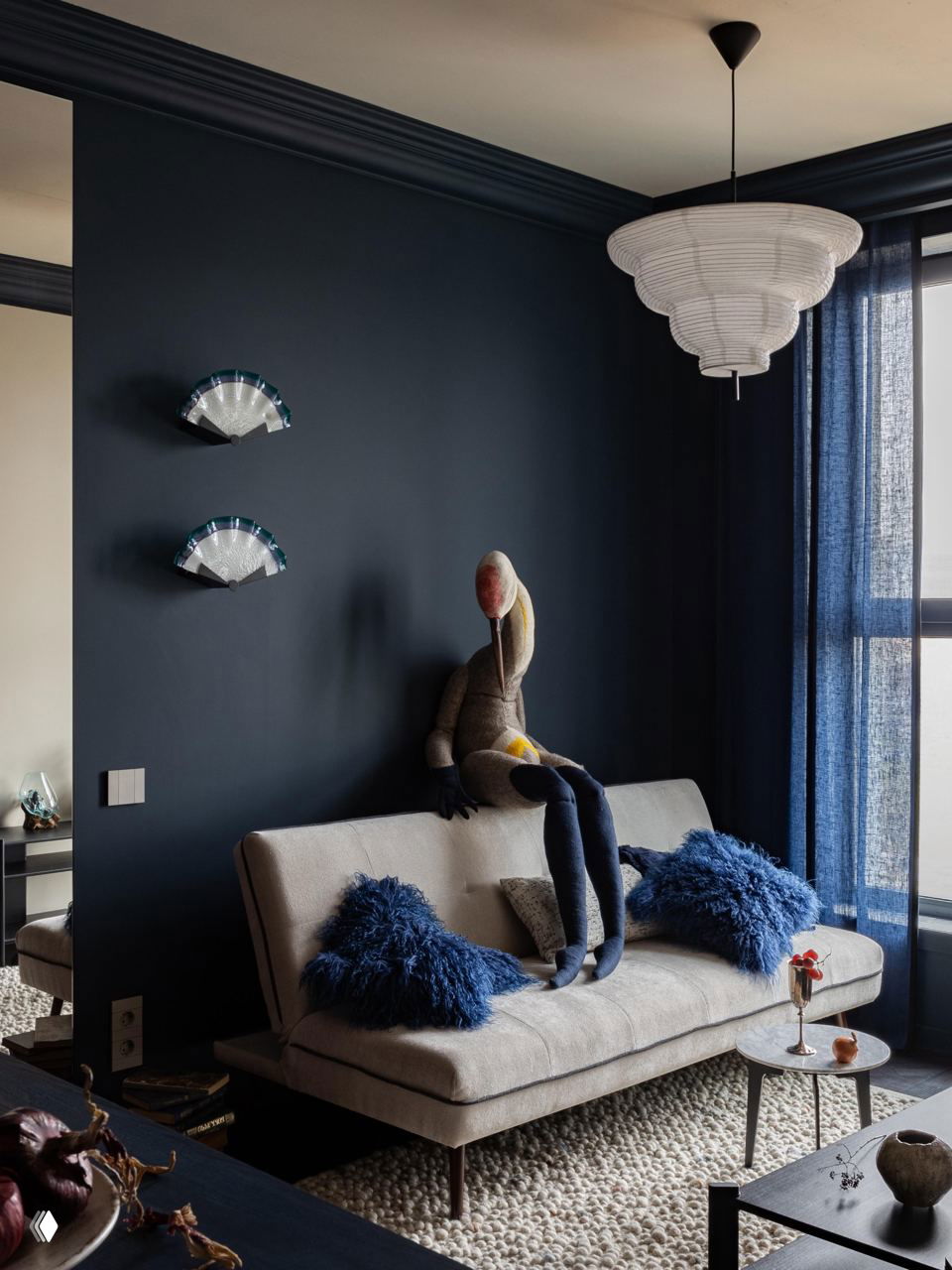 Маленькая зона гостиной с тёмно-синими стенами, серой софой и пушистыми синими подушками; холодные глубокие оттенки делают комнату камерной и уютной.