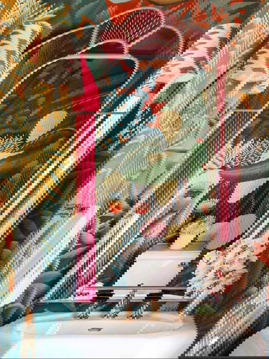 Тропические обои с плотной листвой и изображением обезьяны, видно зеркало, белая раковина и настенные светильники.