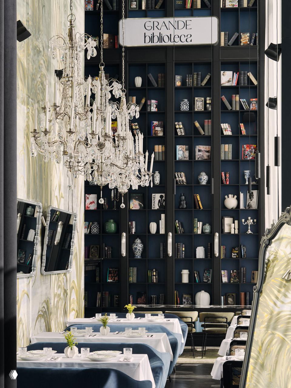 Интерьер ресторана Grande Bibliotheca с очень высокими книжными стеллажами до потолка, хрустальная люстра и сервированные столы с белыми скатертями.