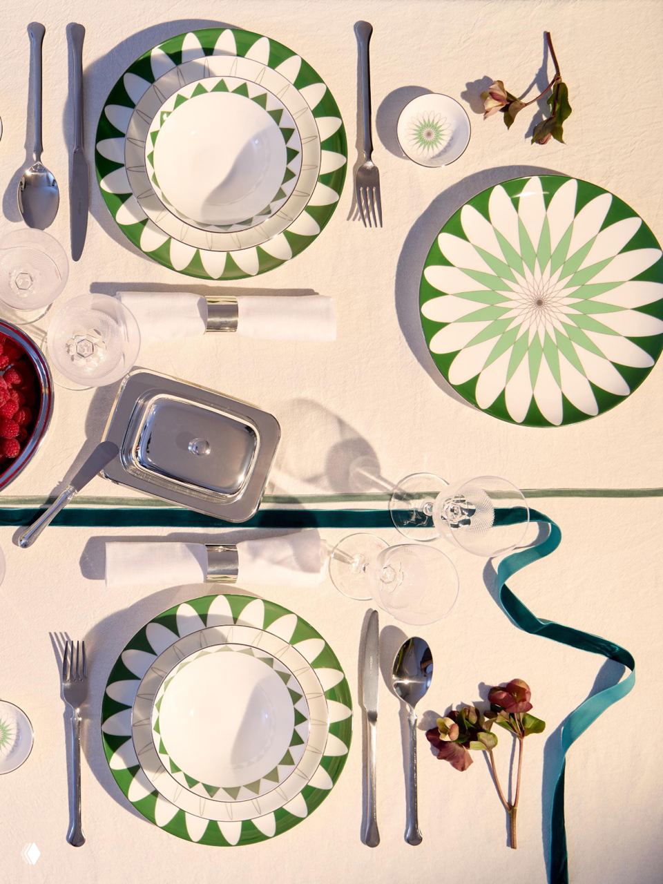 Вид сверху на набор тарелок с повторяющимся зелёно-белым узором, аккуратно расположенные приборы и элементы декора — демонстрация симметрии и рисунка коллекции.