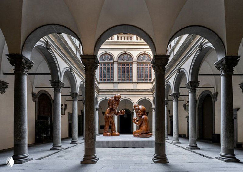 Вид внутреннего двора палаццо Строцци во Флоренции с двумя крупными деревянными скульптурами KAWS на подиуме, окружёнными арочными колоннадами.