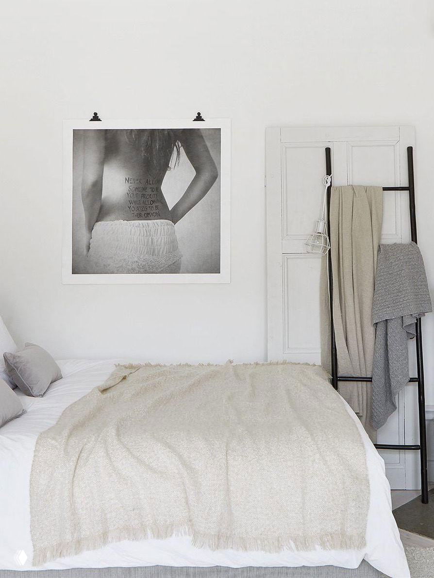 Спальня в светлых тонах с вешалкой‑лестницей у кровати, на которой развешены пледы и одежда — удобная альтернатива стулу.