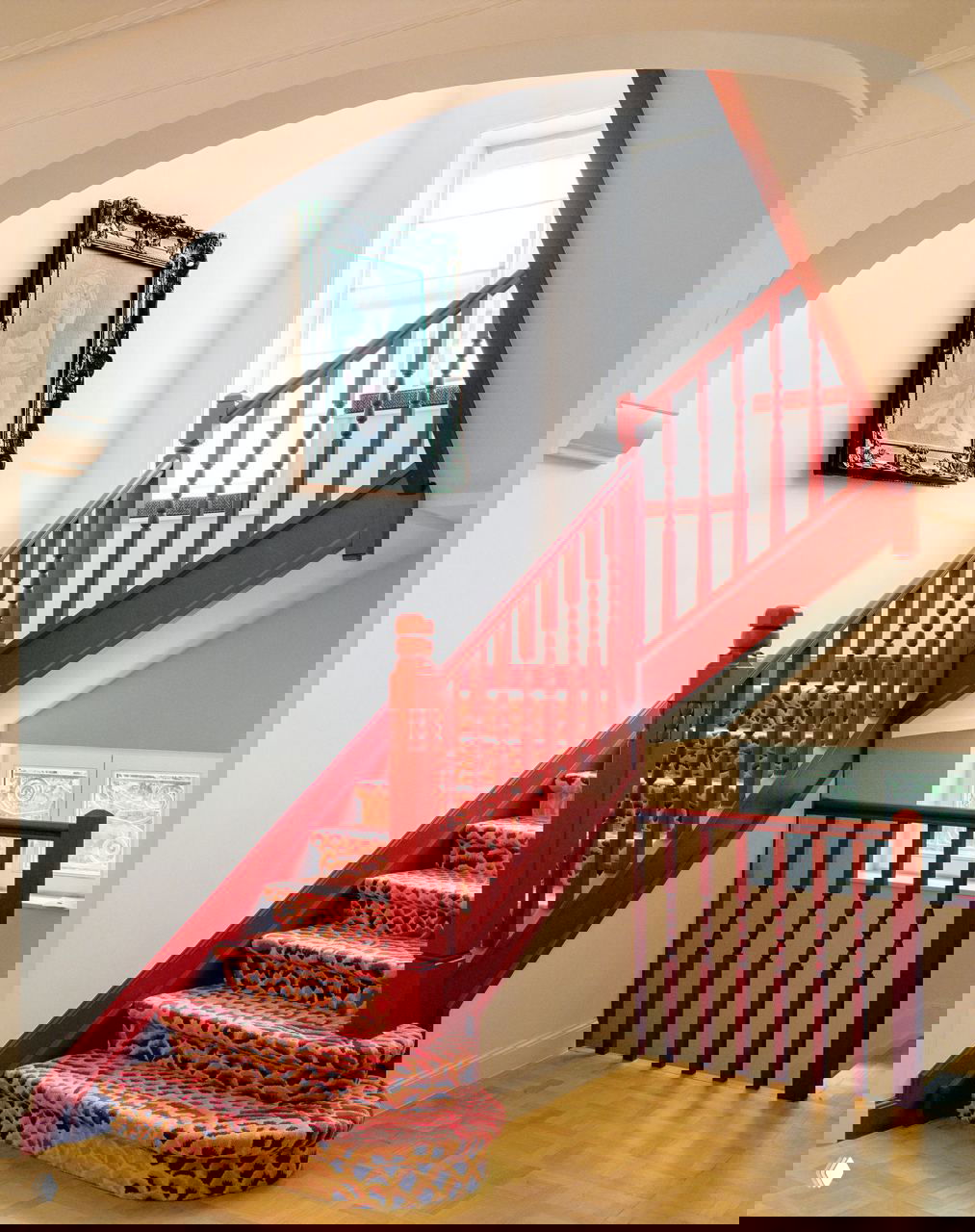 Лестничный пролет с ярко-красной покраской перил и ковровой дорожкой с орнаментом; архитектурные арки подчёркивают исторические детали виллы.