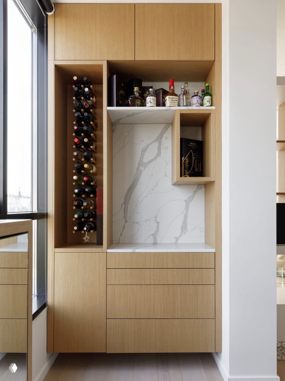 Современный встроенный шкаф из светлого дерева с местом для винных бутылок и полками для алкоголя — лаконичное решение хранения на кухне возле окна.