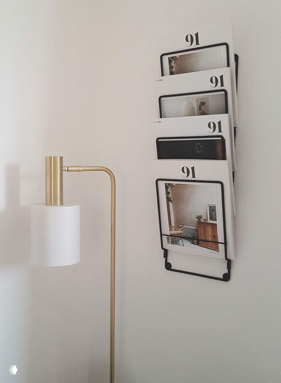 Настенная компактная стойка для журналов рядом со светильником — вертикальное хранение печатных изданий, экономя место на полу и на полках.