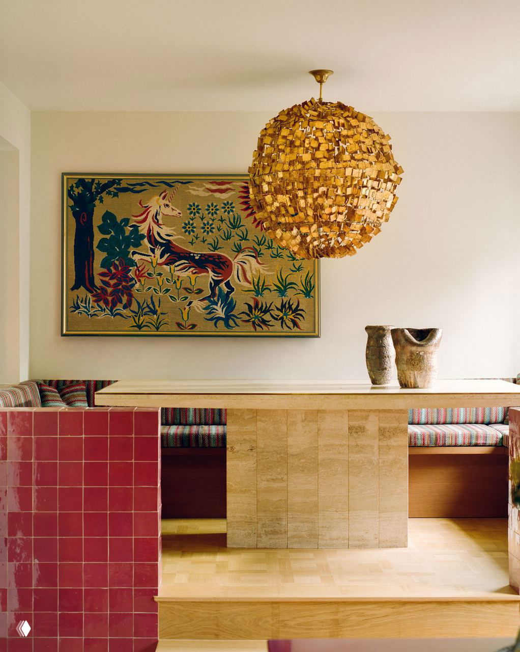 Зона завтраков со встроенной сидячей лавкой в полосатой обивке, розовая марокканская плитка на барной стойке и большая ваза с букетом подсолнухов у круглого окна.