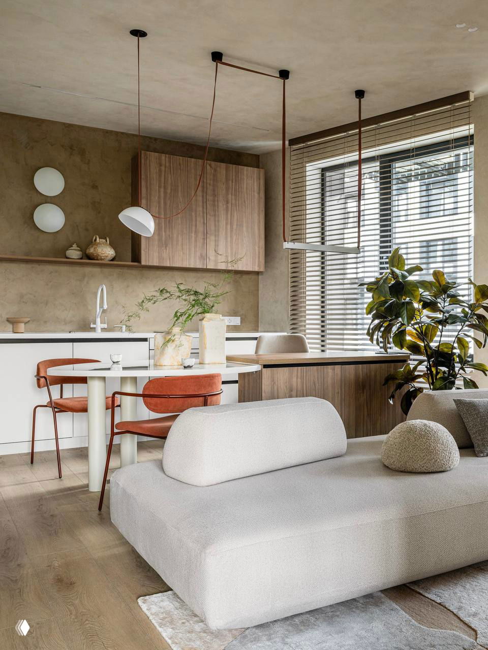Кухня-гостиная в тёплых бежевых тонах с низким белым диваном, округлыми формами мебели, обеденным столом у окна, растениями и деревянными жалюзи.