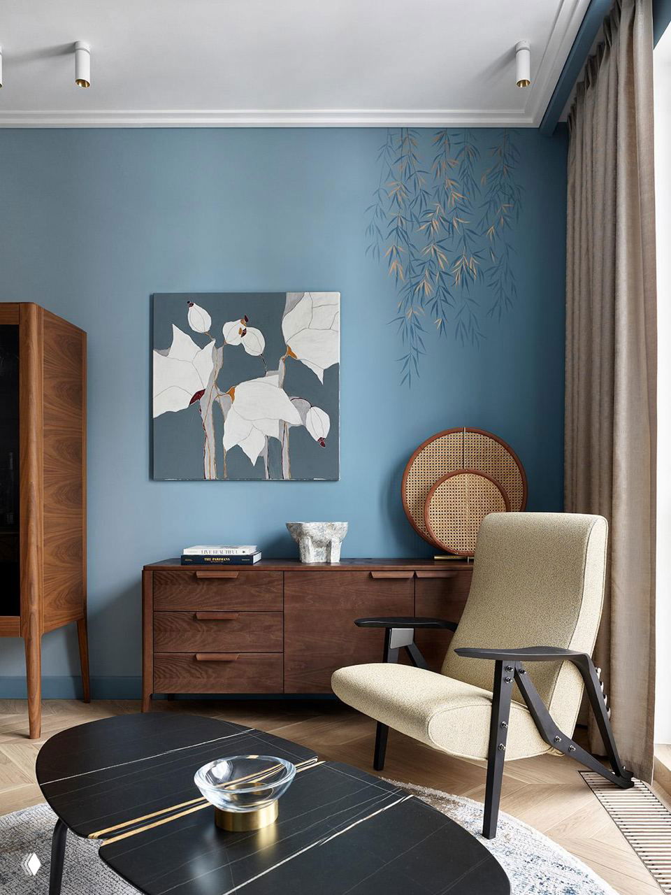 Уютный уголок с деревянной мебелью, синей декоративной картиной и креслом у окна; пастельные холодные стены создают ощущение воздухопроницаемости.